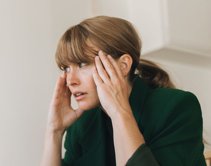 Uma mulher de blazer verde, segurando a cabeça como se estivesse angustiada, depois que alguém brincou sobre bater na filha, nada de bater.