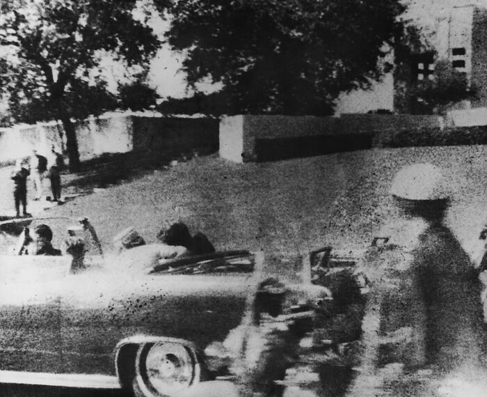 Black and white photo showing a motorcade with soldiers and a convertible car capturing historical moments from the year you were born.