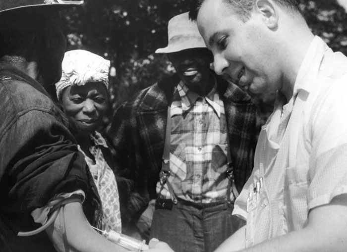 Foto em preto e branco de pessoas interagindo ao ar livre, ilustrando um momento relacionado a grandes traições na história da humanidade.