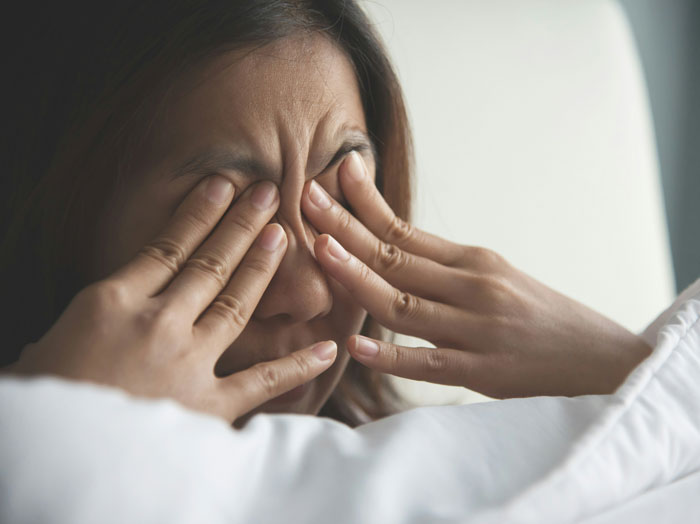 Parent rubbing tired eyes in bed after oversleeping, feeling stressed and overwhelmed with parenting challenges.