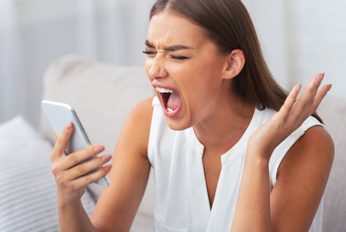 Woman in a white top angrily yelling at her smartphone, expressing frustration related to petty karma and bosses.