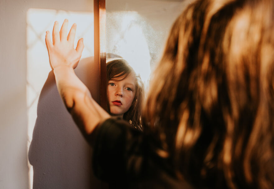 Young girl looking into mirror with serious expression, illustrating the golden child syndrome and its emotional impact.