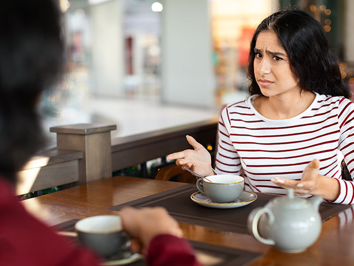 A woman with a distressed expression, gesturing with her hands while on a first date. She wears a striped shirt.