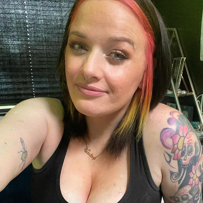 Mulher com cabelo rosa e laranja e tatuagens, retrato de selfie relacionado aos restos mortais de uma mãe desaparecida encontrada por caminhantes.