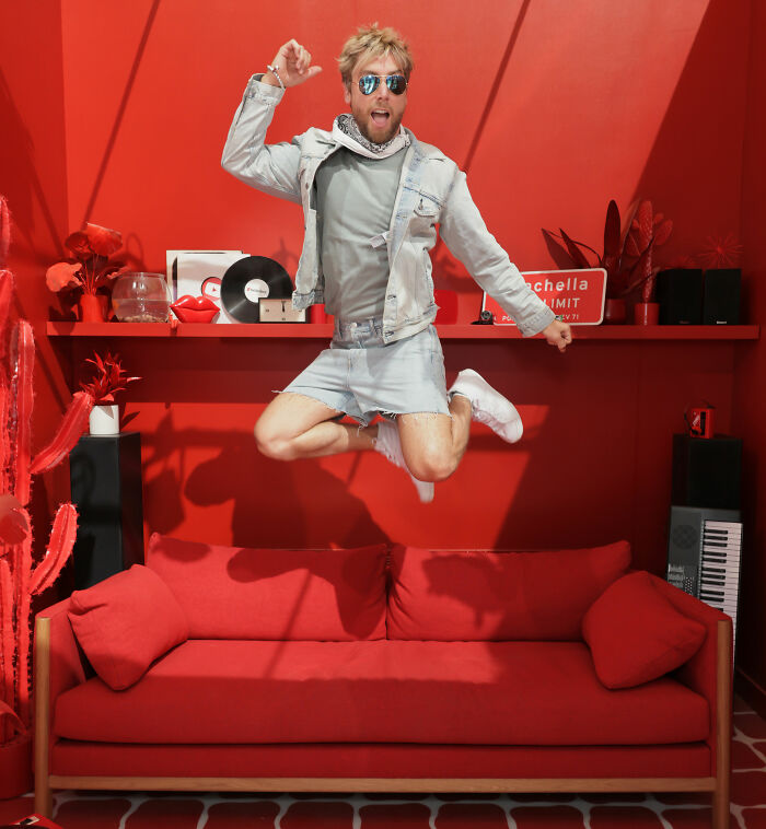 Man wearing a denim jacket and skirt combination jumps in a red room showcasing Coachella Weekend 2 fashion fails.