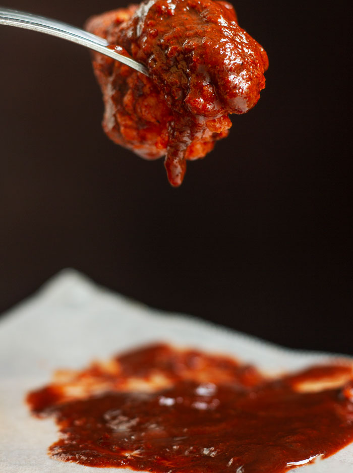 Spicy red sauce drips from a spoon onto white parchment paper, symbolizing a favorite thing about Black people.