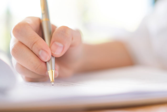 A person's hand holding a pen, writing on paper, capturing those dumb dating moments.