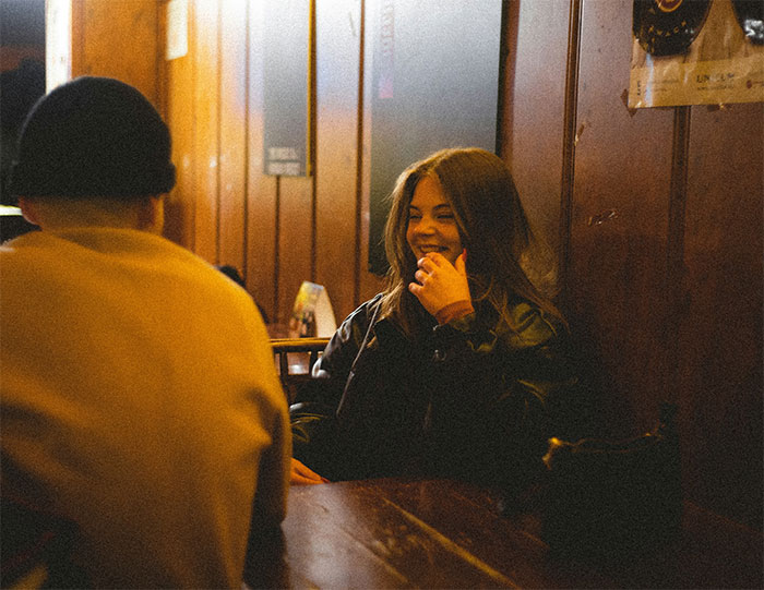 Woman sharing a crazy story about her mom, smiling and talking in a cozy wood-paneled room with a companion.