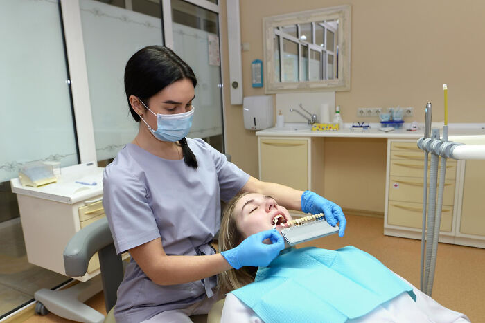 Dentist examining patient's teeth while comparing dental shades during a routine body health checkup.