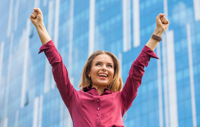 Young woman in a red shirt raising her arms triumphantly, representing inspiring comebacks and thriving success outdoors