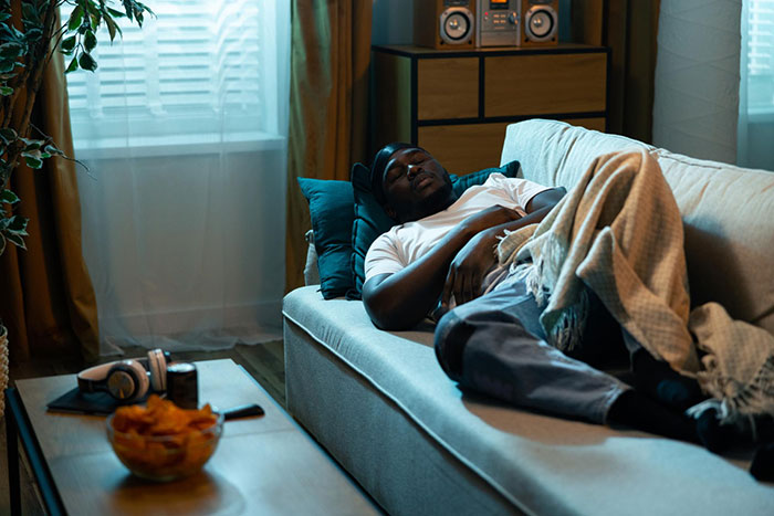 Man sleeping on a couch, headphones and chips on a coffee table. This scene suggests relaxation, a break from messy fights.