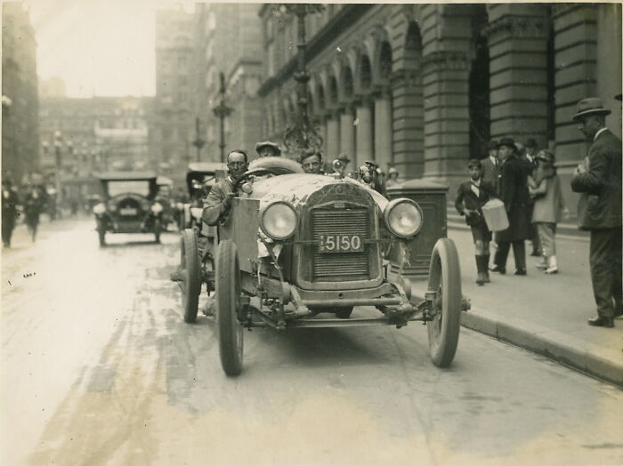 Early 20th century rare and interesting photo of a vintage race car driving through a city street with onlookers.