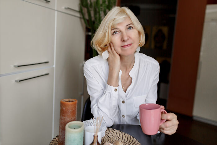 Blonde woman sitting at table holding pink mug, reflecting on first dates with red flags and instant regret.