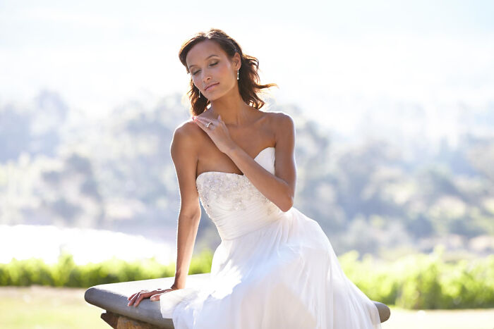 Bride in a white wedding dress sitting outdoors, reflecting the mood of guests witnessing a future breakup at a wedding.