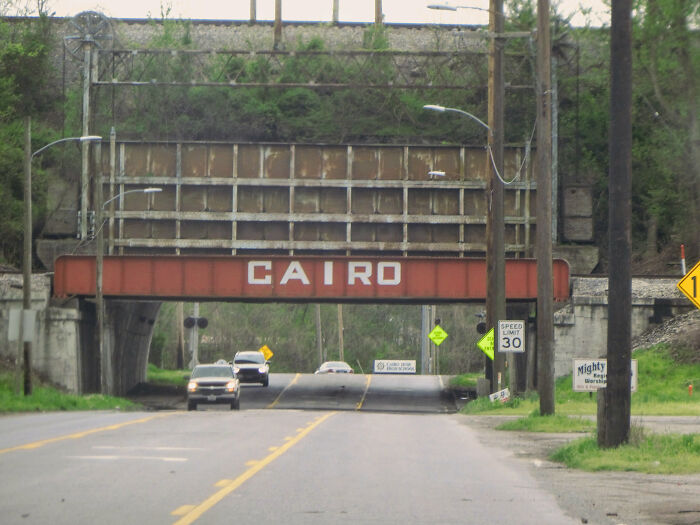 Rusty railroad bridge over road with cars passing beneath, representing one of the worst places in the US visited.