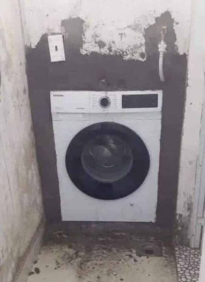 A weird image of a washing machine improperly installed in a narrow, unkempt space, illustrating "weird images".