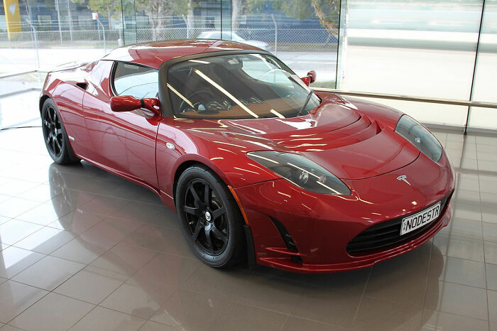 Red Tesla sports car parked indoors with black wheels, showcasing sleek design and modern electric vehicle features.