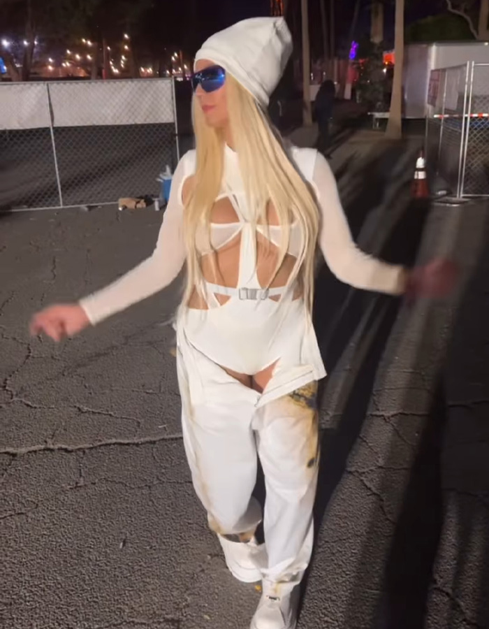 Heidi Klum in an unrecognizable Coachella 2026 look wearing a white cutout outfit, beanie, and blue sunglasses at night.