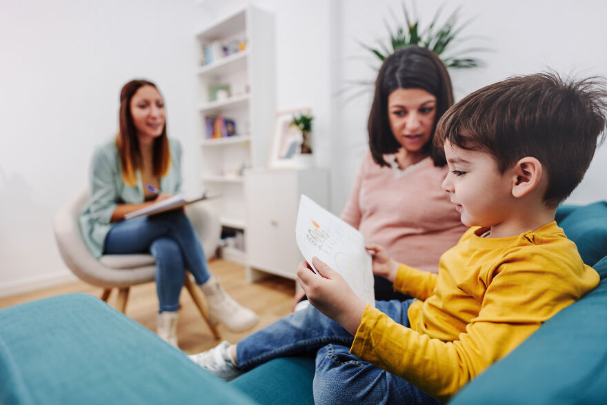 Child in yellow shirt showing a drawing to a woman on a couch during a therapy session about golden child syndrome.
