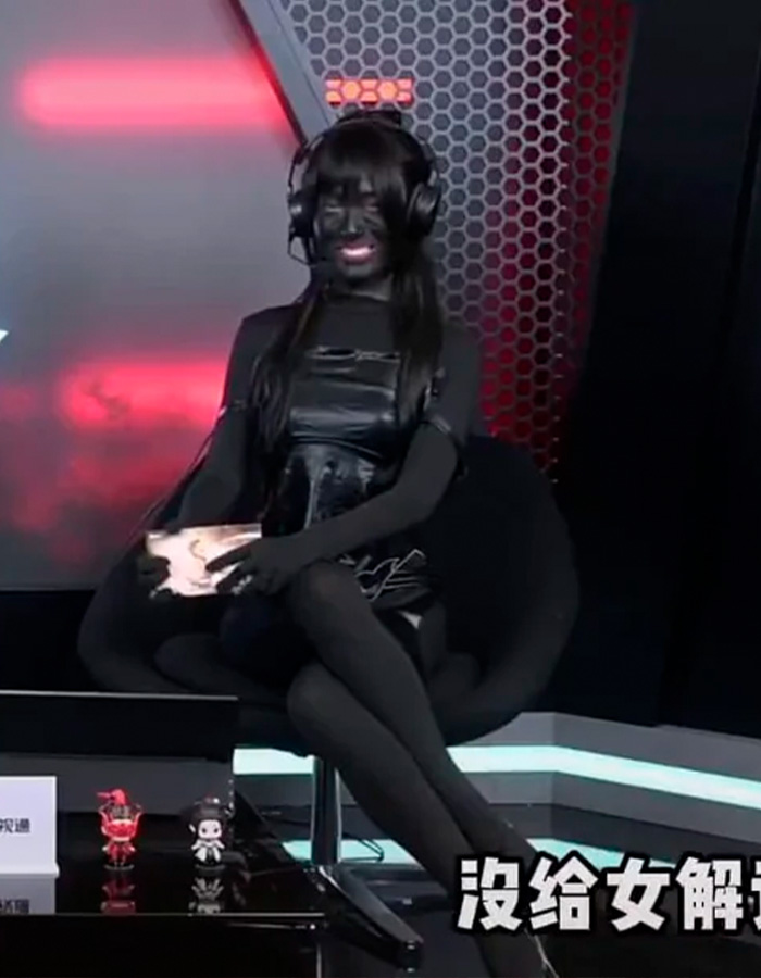 Esports host seated in black outfit and headset, responding to trolls about her revealing outfit during a live broadcast. Esports host seated in black outfit and headset, responding to trolls about her revealing outfit during a live broadcast.