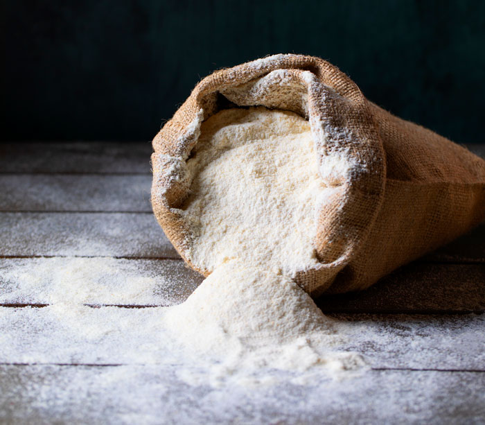 A burlap sack overflowing with white flour onto a rustic wooden surface, revealing interesting facts about the world.