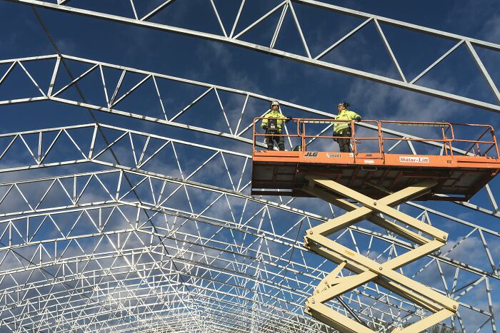 Construction workers on a scissor lift installing metal framing for a building. Represents workplace incidents and safety.