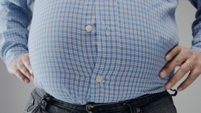 An overweight man's belly straining the buttons of his blue plaid shirt. A gross office story of shared workspace challenges.