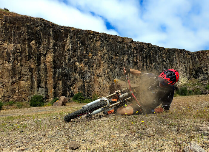 A mountain biker in a red helmet crashes, dust flying, in a rocky landscape. An example of what it really costs them.