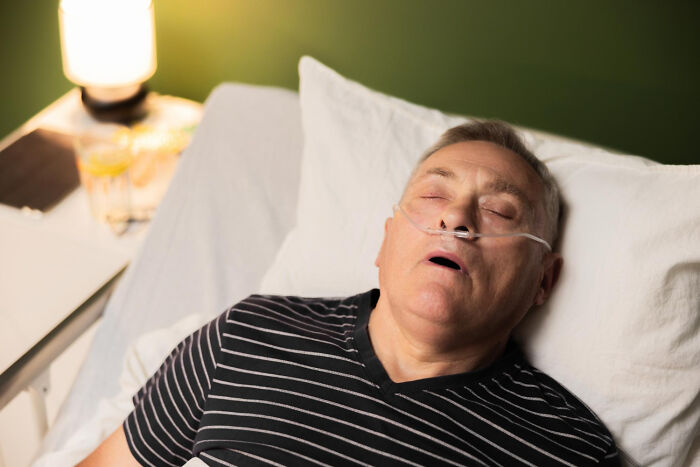Older man with nasal oxygen asleep in hospital bed, illustrating hidden truths about hospitals that may scare patients.