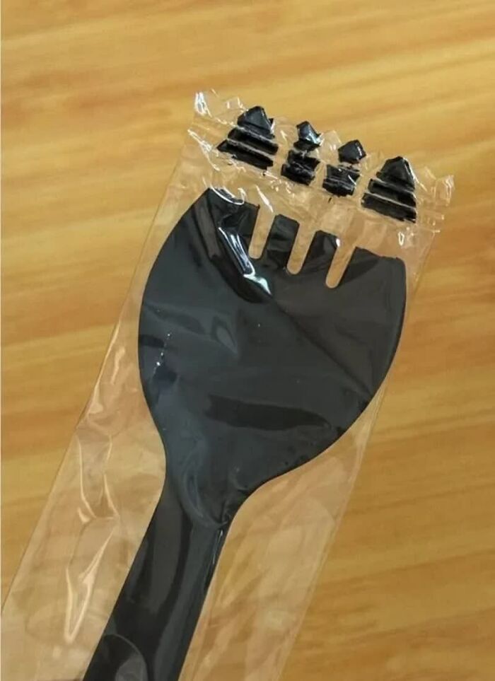 A weird image of a black plastic spaghetti server in a clear plastic wrapper, with the prongs extending outside the seal.