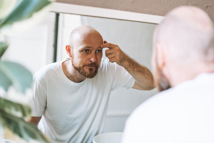 Man examining his face closely in front of a mirror, reflecting on random facts people learned about their bodies.