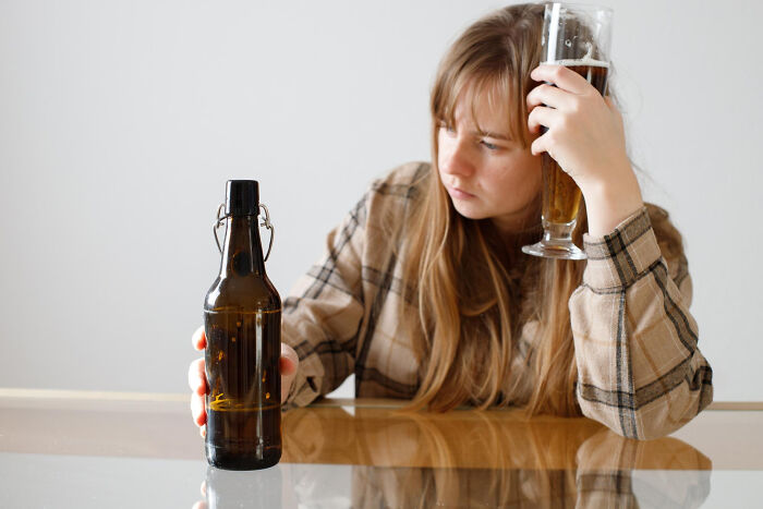 Young woman holding beer glass and bottle, looking disappointed and regretful after a disastrous first date with red flags.