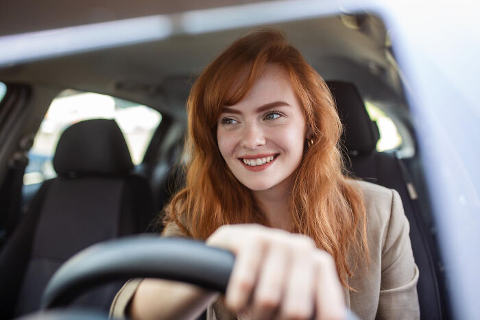 Young woman with red hair smiling confidently while driving, illustrating inspiring comebacks and thriving success moments.
