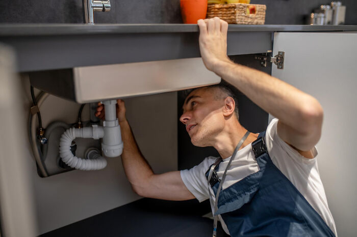 Plumber working under a sink fixing pipes, demonstrating a skilled job that AI can’t touch in building maintenance.