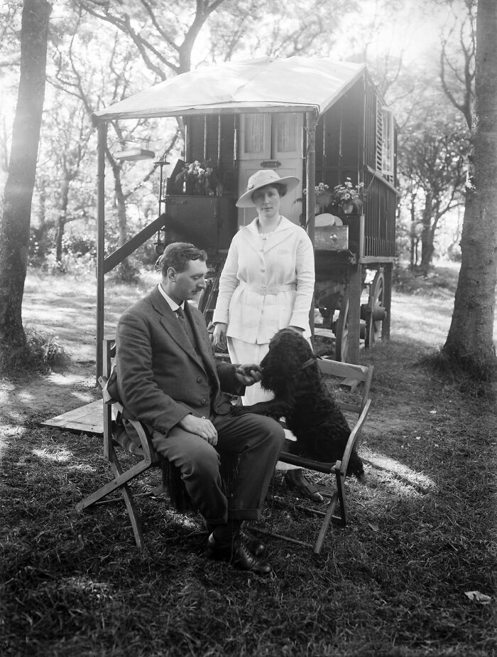 Early 20th century rare and interesting photo of a man, woman, and black dog by a vintage caravan in a wooded area.