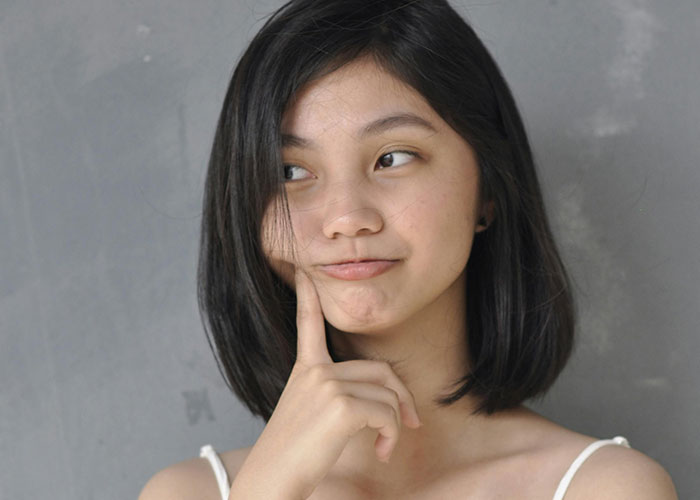 Jovem de cabelo preto com aparência contemplativa, representando a mãe que resolve o problema com as próprias mãos pelo filho.