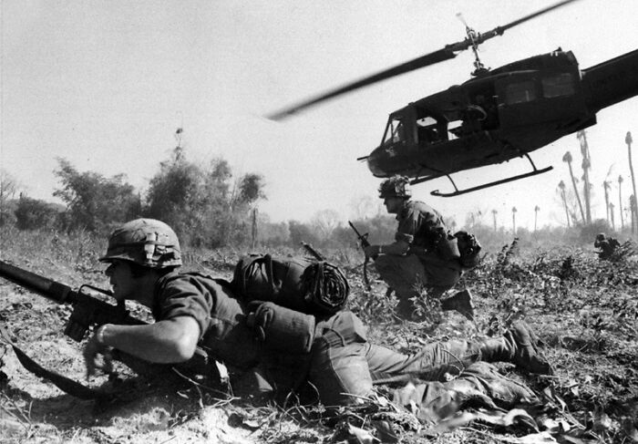 Soldiers taking cover in a field with a helicopter overhead, depicting a historic moment from the year you were born.