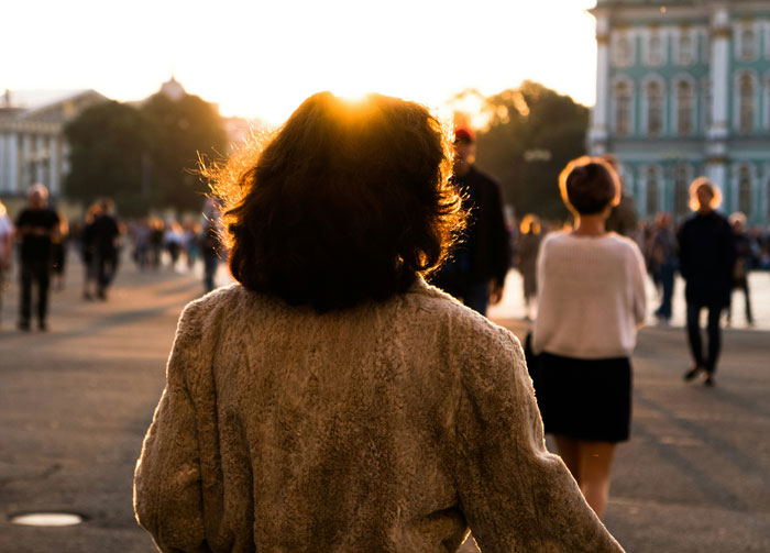Woman walking outdoors at sunset among a crowd, representing things women are tired of explaining to men.