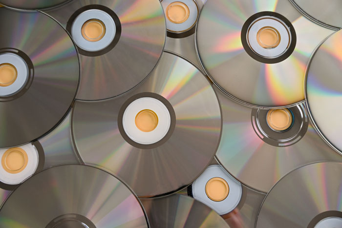 Multiple overlapping shiny CDs reflecting light, symbolizing petty karma served to bosses in satisfying ways.