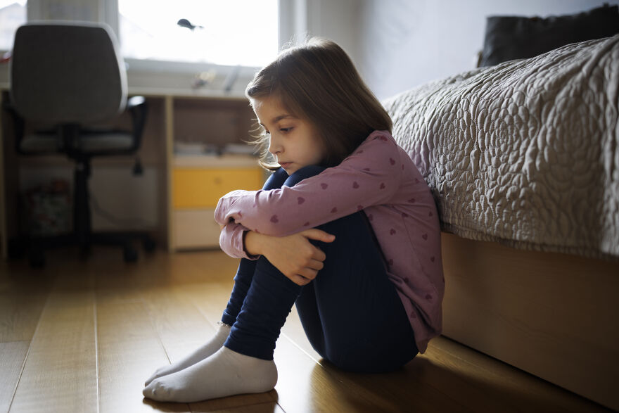 A young girl sitting alone on the floor, looking sad and contemplative, illustrating golden child syndrome struggles.