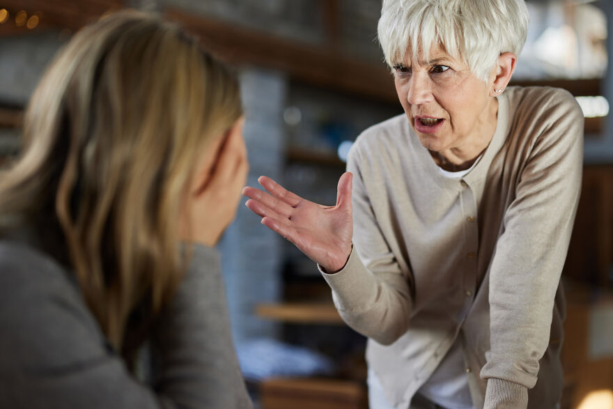 Older woman expressing frustration to younger woman covering face indoors, illustrating outcast and family narrative conflict.