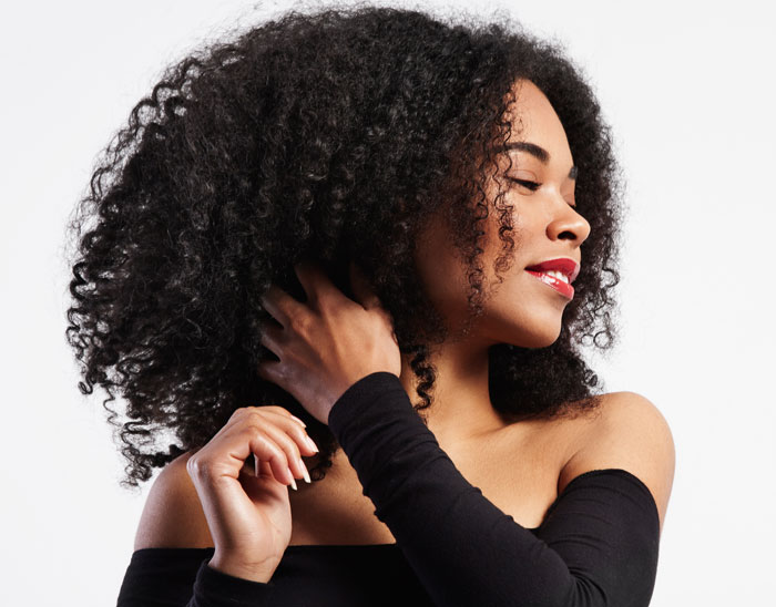 Beautiful young Black woman with curly hair, smiling with red lips and a black off-the-shoulder top.