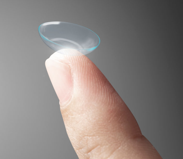 A clear contact lens resting on a fingertip against a gray background. Illustrates gross office stories and sharing a workspace.