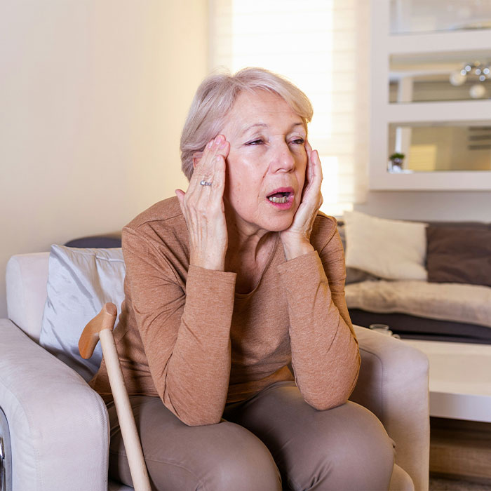 Mulher idosa com cabelos grisalhos, parecendo angustiada, segurando a cabeça. Potencial efeito colateral de comer ovos para tratamento de Alzheimer.