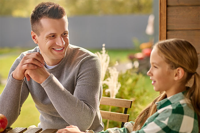 Man and young girl smiling and talking outdoors, illustrating a woman sharing a crazy story about her mom.