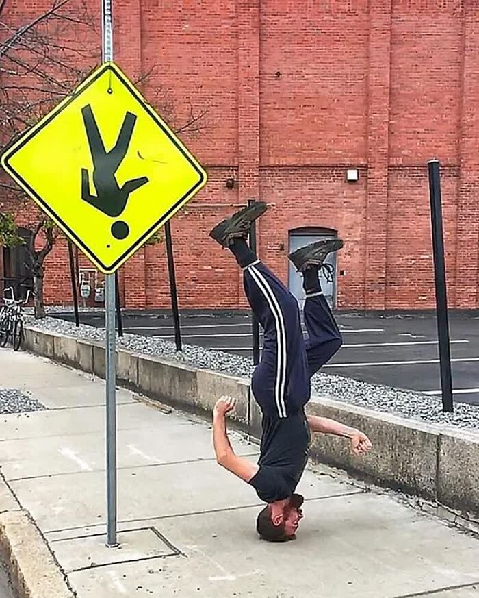 A man doing a headstand next to a yellow sign with an upside-down figure, one of many weird images.