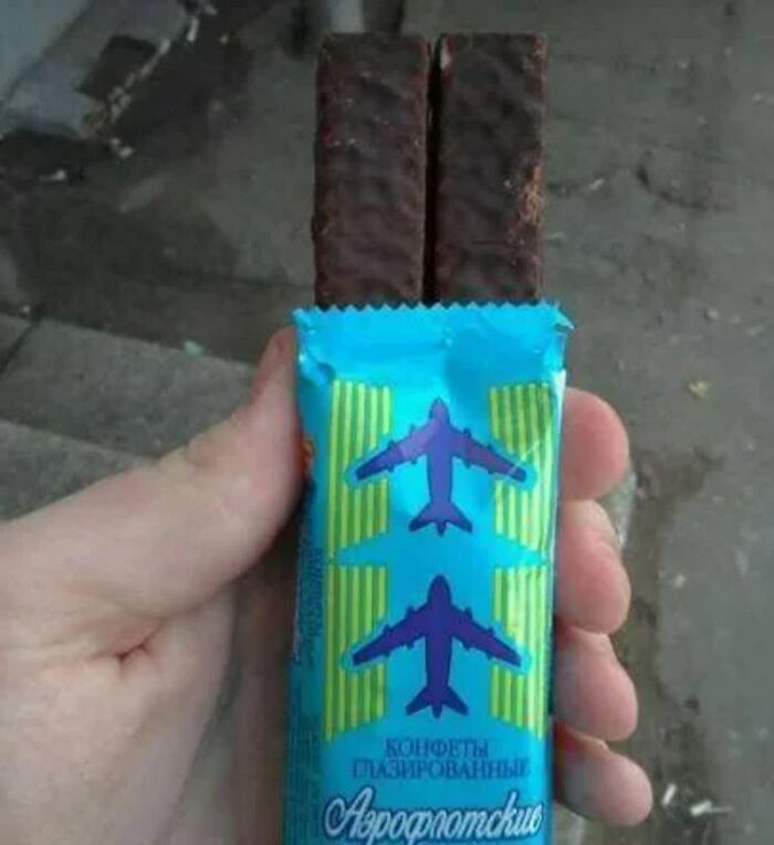 A hand holds a blue candy wrapper with two purple airplanes, revealing two chocolate bars. Weird images.