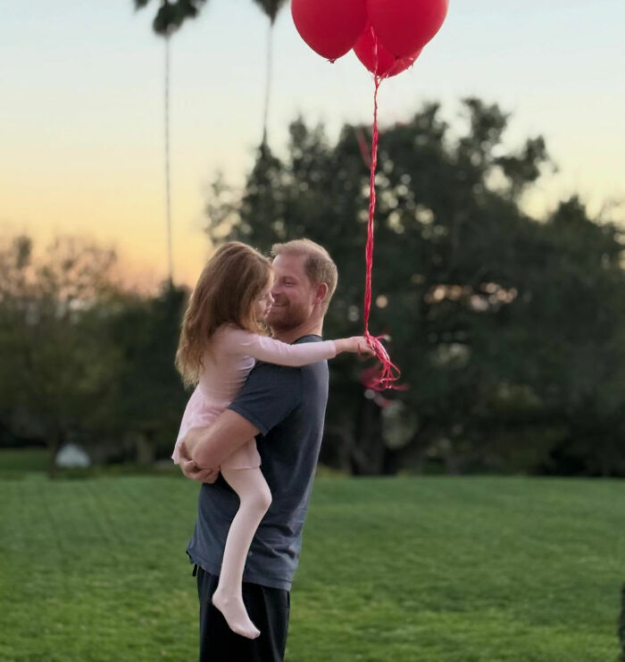 Man holding young girl with red balloons outdoors at sunset, photo linked to Meghan Markle Easter clip backlash.