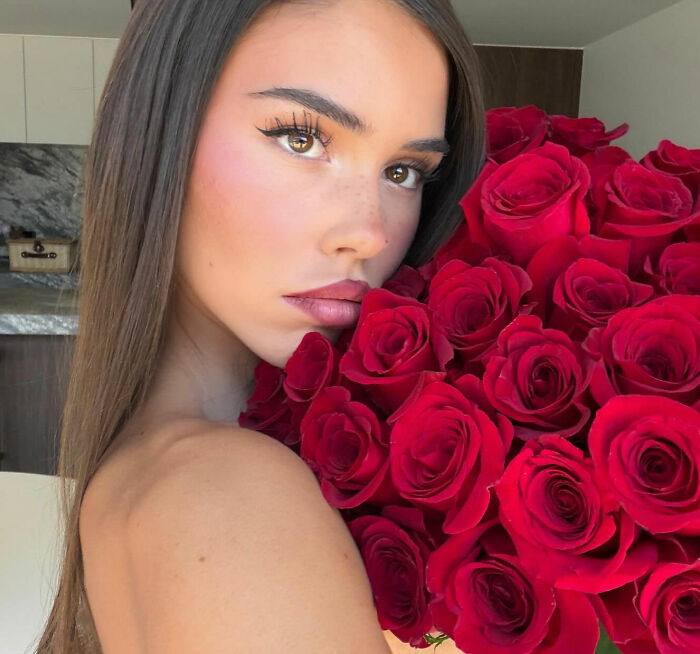 Coachella guest holding bouquet of red roses, turning heads with stunning beauty and glowing natural makeup close-up.