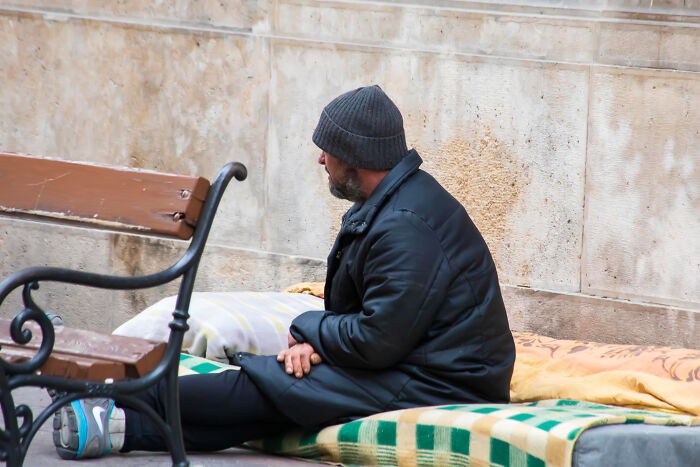 A bearded man in a dark jacket and beanie sits on blankets on the street, illustrating disturbing sounds people heard.
